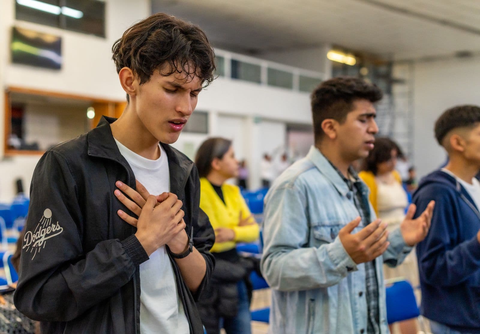 Young people with eyes closed and hands raised or held over their hearts in prayer